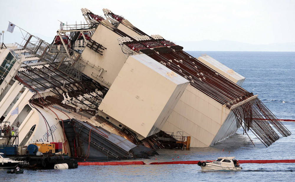 Salvage crew workers are seen in front of  the capsized cruise liner Costa Concordia after the start of the "parbuckling" operation outside Giglio harbour September 16, 2013. Engineering teams began lifting the wrecked liner upright on Monday, the start of one of the most complex and costly maritime salvage operations ever attempted. The operation will see the ship rotated by a series of cranes and hydraulic machines, pulling the hulk from above and below and slowly twisting it upright. REUTERS/Tony Gentile (ITALY - Tags: DISASTER SOCIETY MARITIME TRANSPORT)